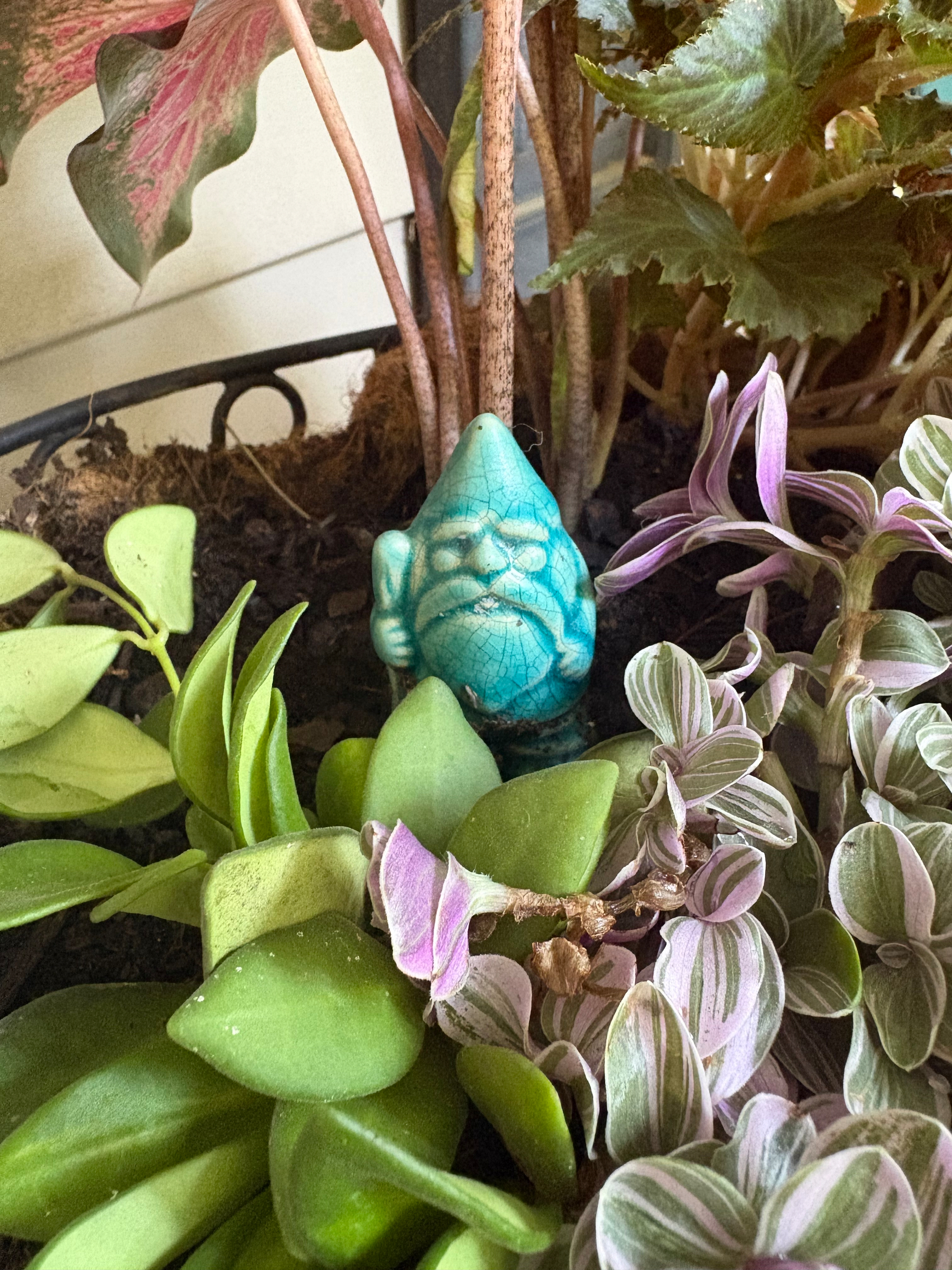 A little gnome standing guard in a flower pot.